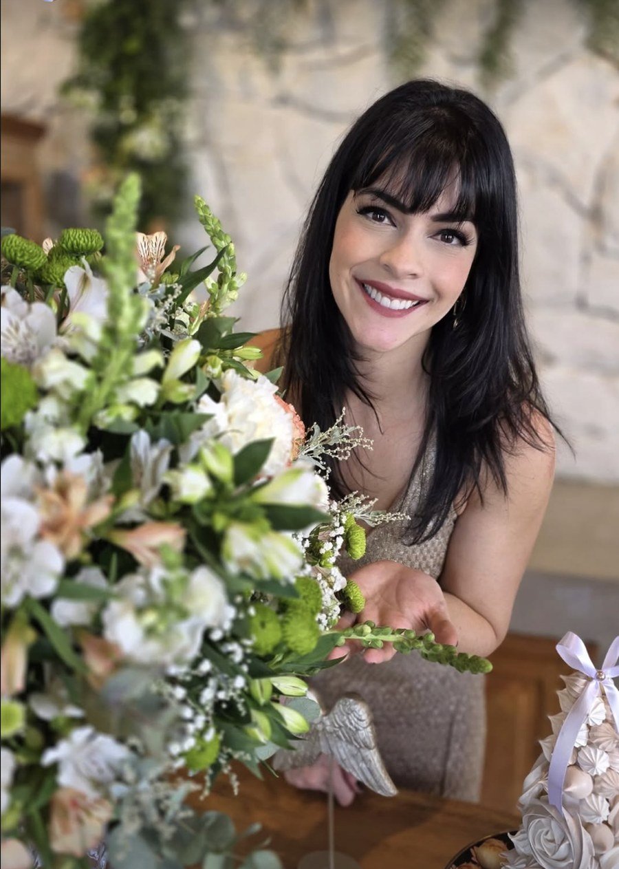 Maju Salloum sorrindo, ajustando um arranjo de flores durante a montagem de uma festa